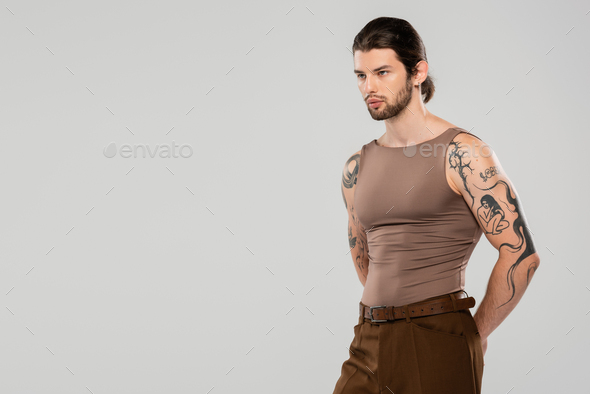 Long haired tattooed man looking away while standing isolated on grey