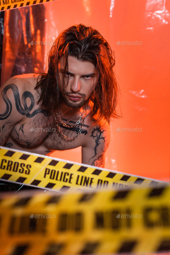 Long haired tattooed man looking at camera near police line