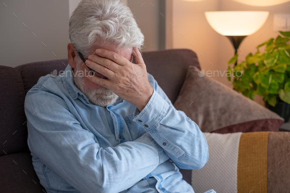 Sad senior man sitting at home with hand over his face feeling lonely and depressed