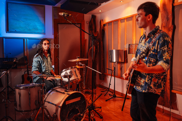 Guitar player and drummer experimenting before recording session in music studio.