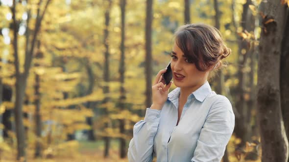 Woman with cellphone in park. Girl speaking on mobile phone in the autumn forest alt