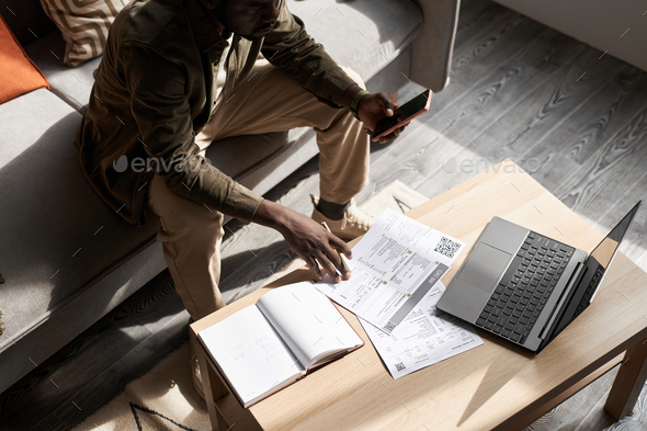 Black man doing taxes at home in sunlight with financial documents on table