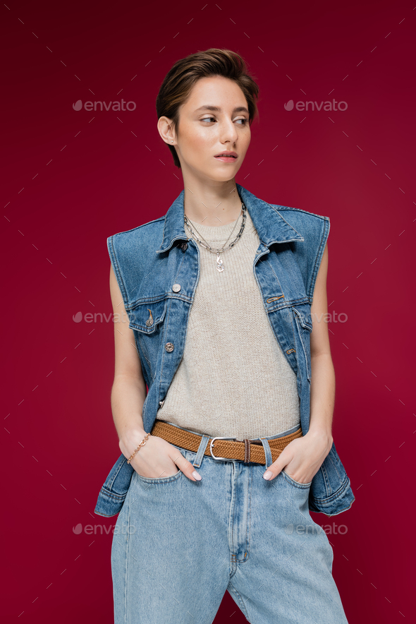 young model in denim vest standing with hands in pockets on dark red background