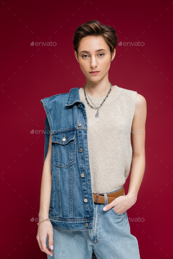 pretty young model in denim vest standing with hand in pocket on dark red background