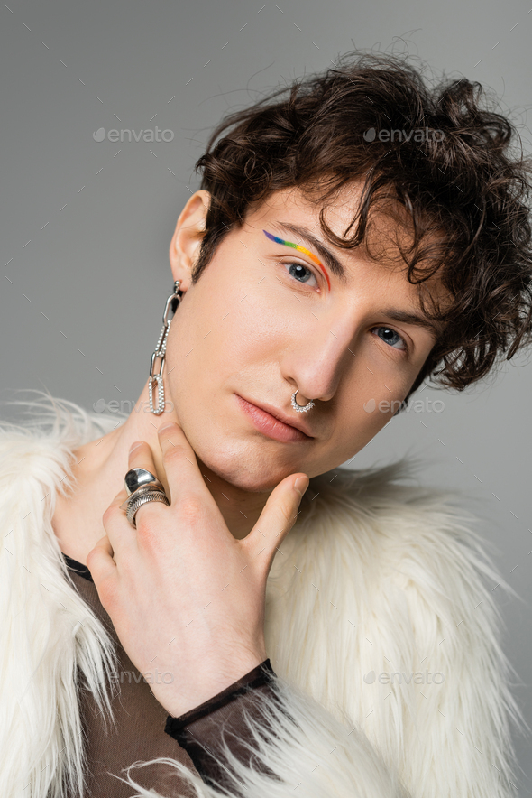 portrait of pansexual model with wavy brunette hair and rainbow eye liner looking at camera isolated