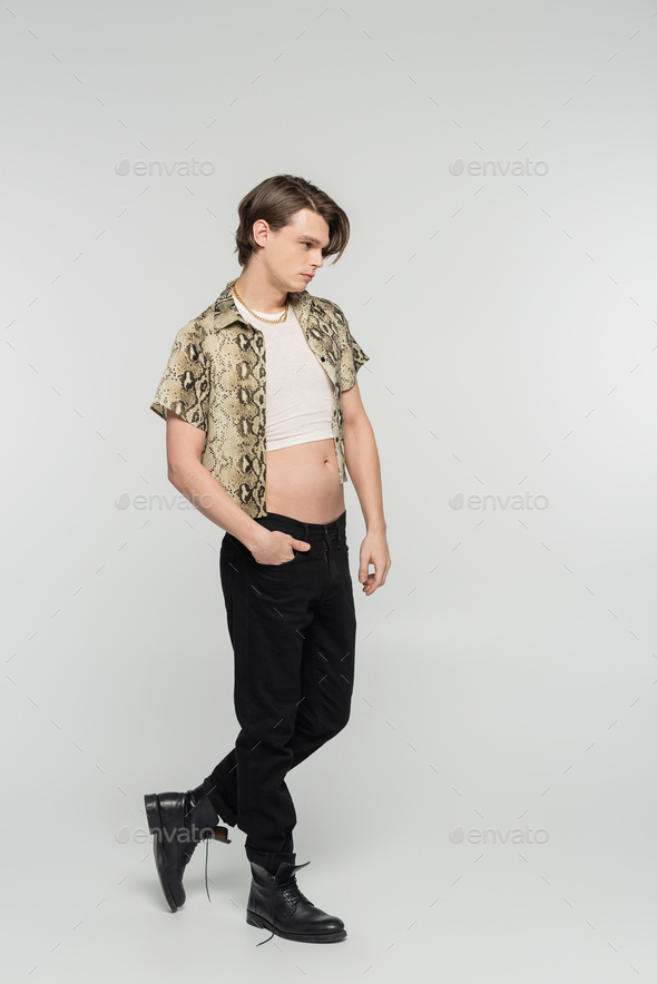 full length of pansexual person in snakeskin print blouse and black trousers posing with hand in