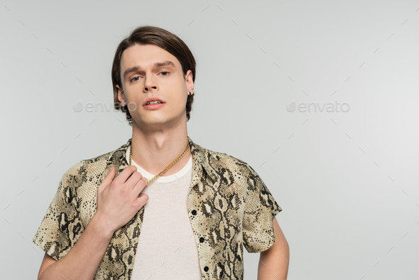 young nonbinary person in snakeskin print blouse touching golden necklace and looking at camera