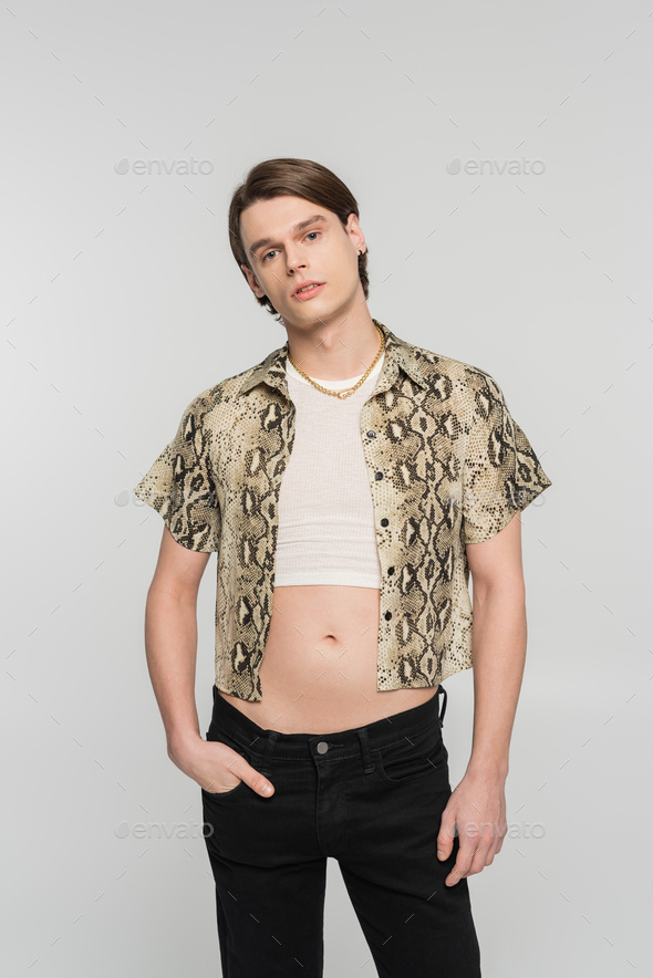 stylish bigender person in snakeskin print blouse posing with hand in pocket of black pants isolated