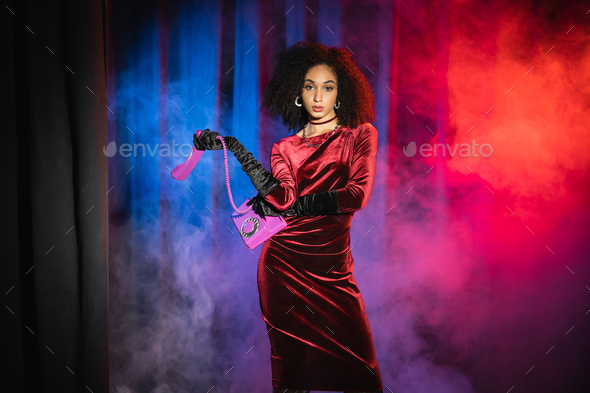 Young african american model in velvet dress and gloves holding