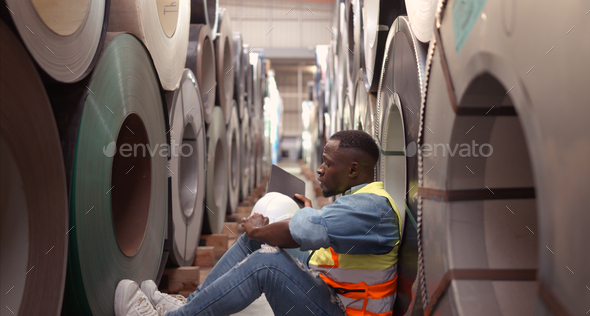 A young man works in a warehouse storing rolls of metal sheet material.