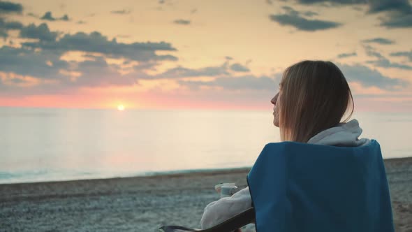 Young Woman Drinking From Thermos and Sitting on Camping Chairs on the Beach alt