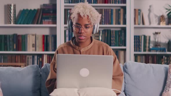 African Woman in Headset Looking at Laptop Holding Web Call with Colleagues alt