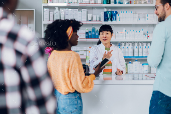 Japanese woman pharmacist selling drugs to a diverse customers in a pharmacy