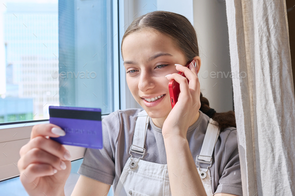 Teenage girl with credit bank card talking on cell phone at home