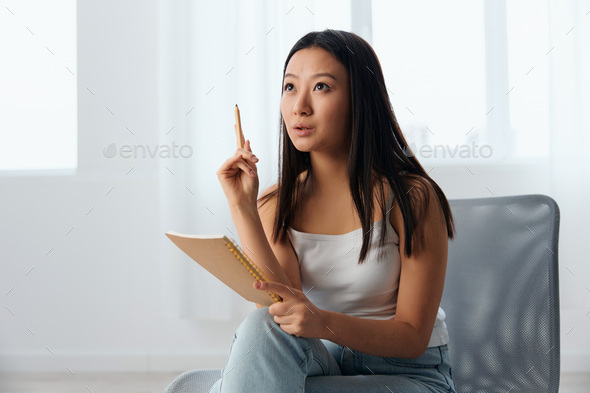 Dreaming excited happy young brunette have cool idea insight holds pen up and notebook in hand looks