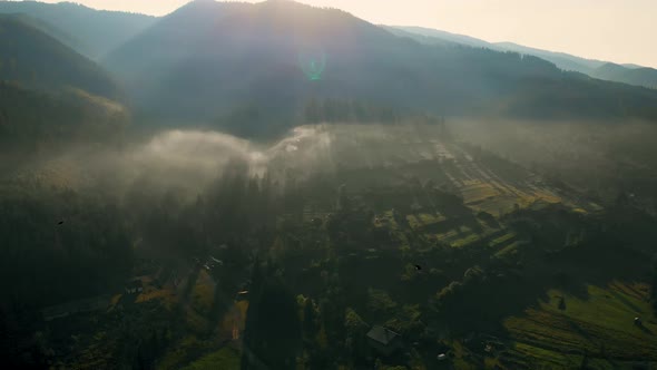 Aerial view of sunrise over foggy village in mountains.