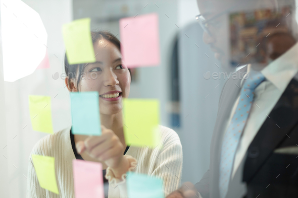 Happy multiethnic business team meeting pointing at post it notes on glass board.