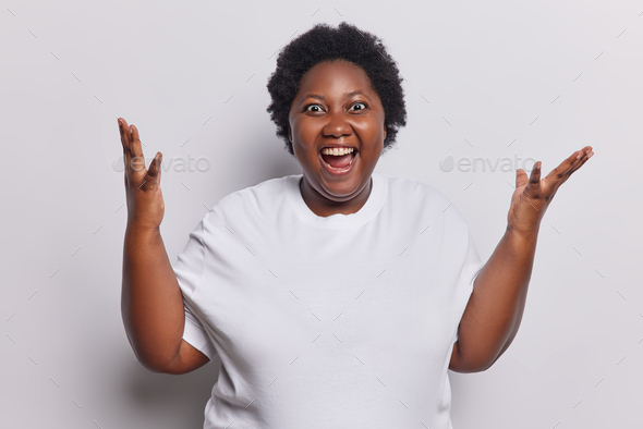 Waist Up Shot Of Emotional Dark Skinned Woman With Curly Hair Keeps Arms Raised Up Exclaims 7036