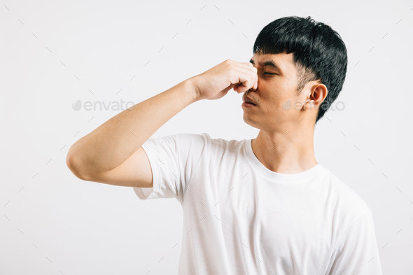 Asian man wearing an anxious expression while pinching his nose due to a strong and stinky odor
