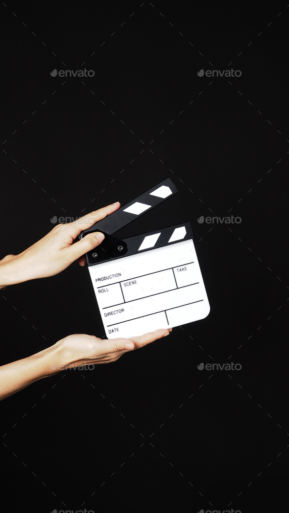 Hand is holding small white clap board or movie slate on black background.