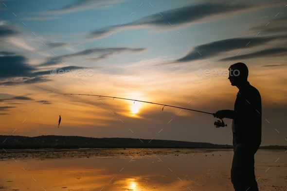 A fisherman silhouette fishing at sunset. Freshwater fishing, catch of fish.  Stock Photo by sedrik2007