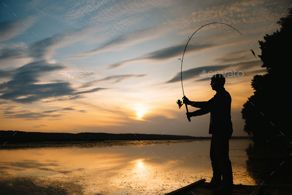 A fisherman silhouette fishing at sunset. Freshwater fishing, catch of fish.  Stock Photo by sedrik2007