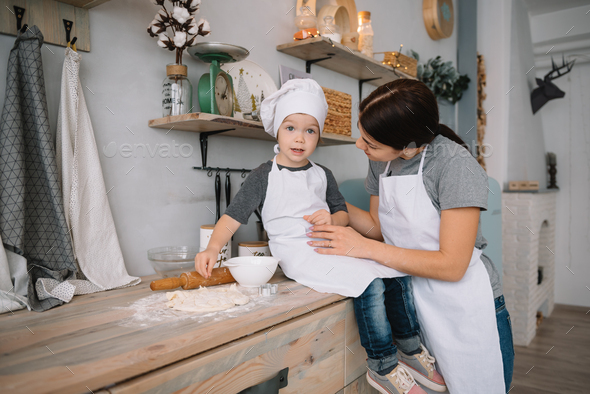 Adorable little boy and his mom in white aprons cooking together in the  kitchen Stock Photo