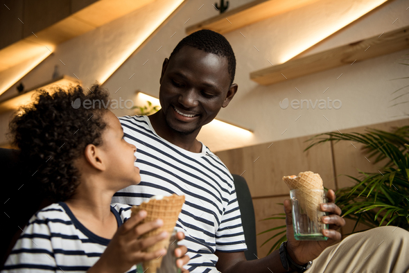 Happy African American Father And Son Eating Ice Cream And Smiling Each