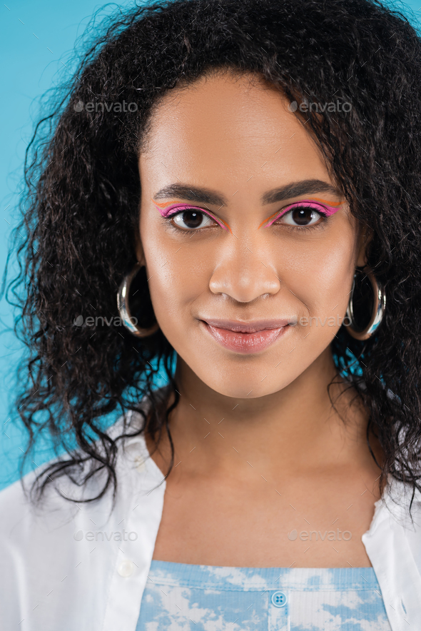 portrait of positive african american woman with curly hair and hoop earrings isolated on blue