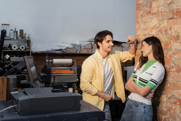 cheerful man flirting with pretty colleague while standing together in print center