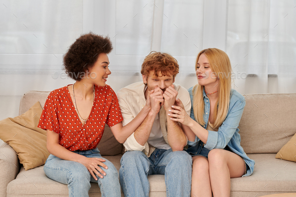polyamorous relationship, cultural diversity, redhead man sitting on couch with happy multiracial