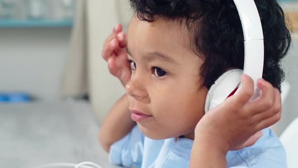 Little African Boy Putting on Headphones and Listening to Music on Smartphone