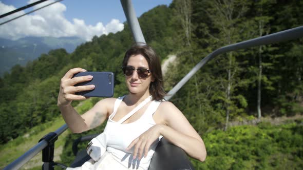 Beautiful Brunette Girl Makes Selfie and Sitting on Funicular or Cable-railway in Mountains in alt
