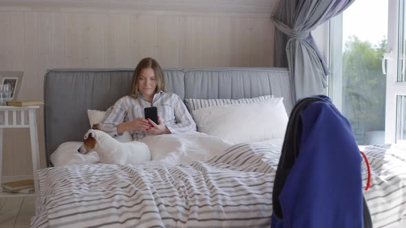 Woman Relaxing in Bed in Morning and Using Phone alt