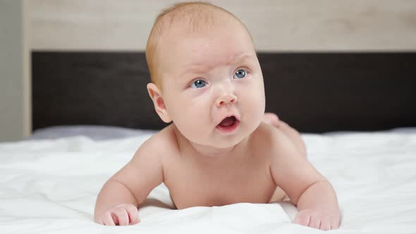 Cute Baby Girl Frowns Trying to Raise Up Head Lying on Bed alt