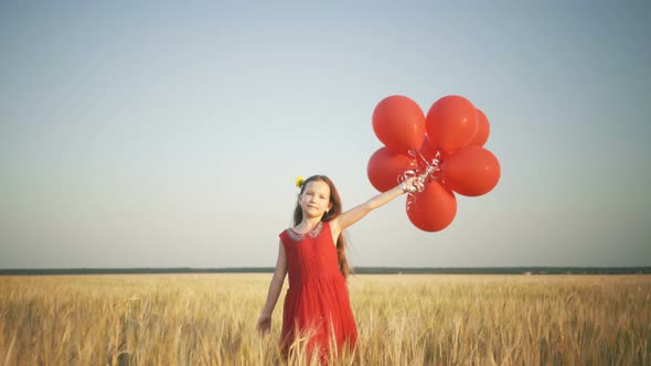 Happy Young Girl with Balloons Running in the Wheat Field at Sunset alt