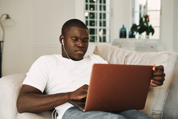 a man lies on the couch with a laptop in headphones technology