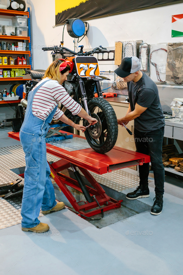 Mechanic team adjusting motorbike wheel on factory