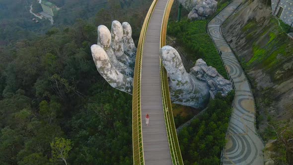 Aerial shot of a young woman walking on the Golden Bridge in the city of Danang alt