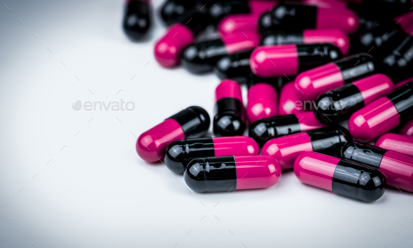 Pink-black capsule pills on white table. Antibiotics drug resistance. Global healthcare. Antibiotic