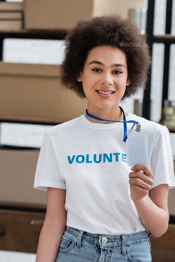 smiling african american woman holding blank name tag in volunteer center