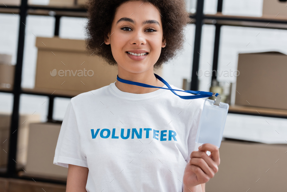 cheerful african american volunteer showing blank id card in donation center