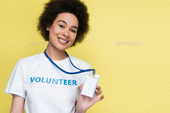 african american volunteer smiling at camera and showing blank id card isolated on yellow