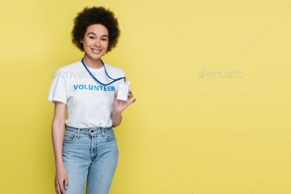 african american volunteer smiling at camera and showing blank id card isolated on yellow