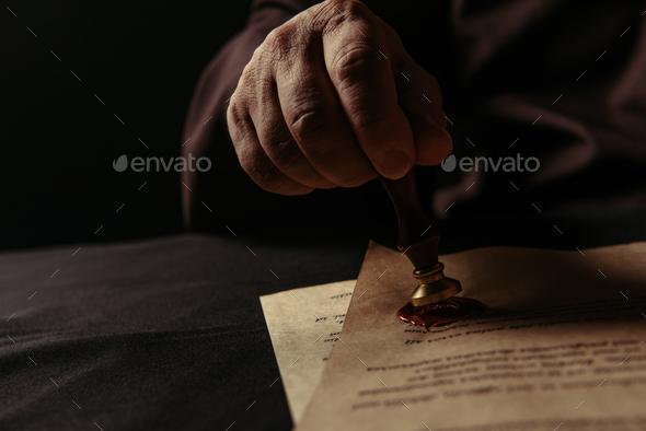 cropped view of abbot holding wax seal near parchment with chronicle isolated on black