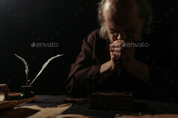 medieval monk praying at night near cross and holy bible isolated on black