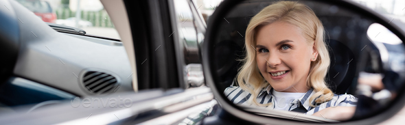 Cheerful blonde woman reflecting in blurred mirror of auto, banner