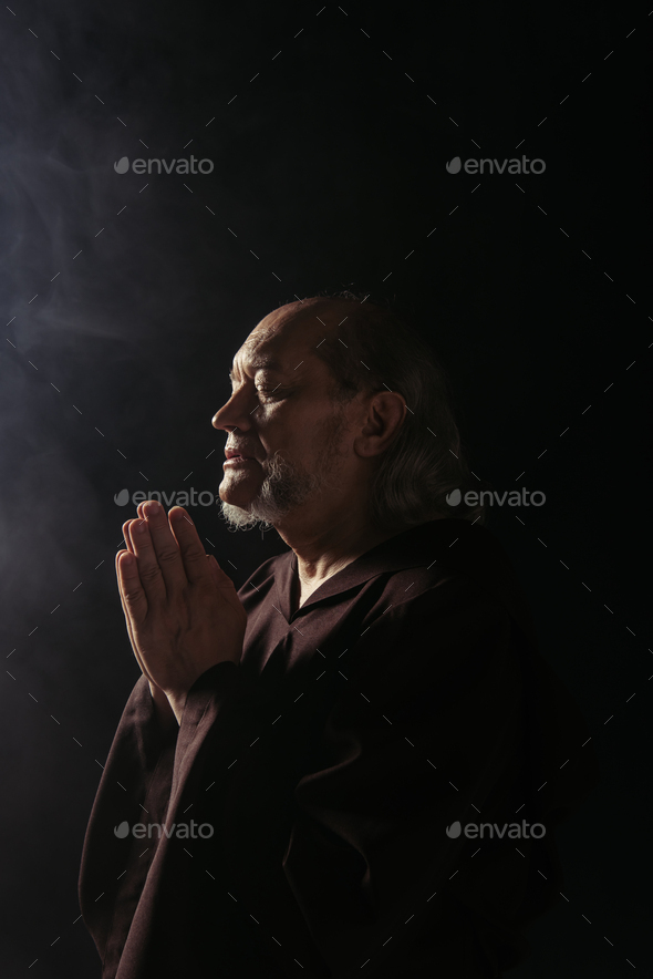 medieval priest with closed eyes praying at night on black background