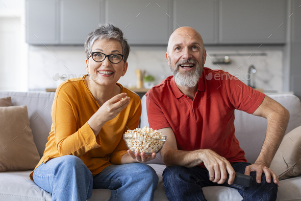 Happy Married Senior Couple Watching Tv And Eating Popcorn At Home
