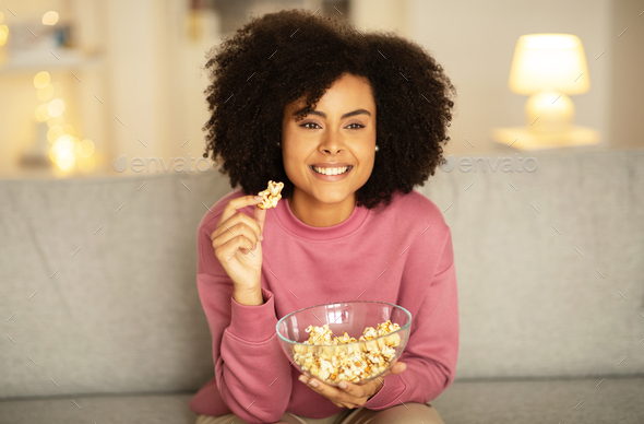 African American woman enjoying film on TV, munching popcorn indoor